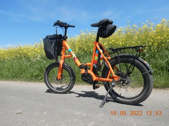 Havergoh Hotel_adfc ISY Pedelec.JPG Ein leuchtend oranges Pedelec steht einsatzbereit auf einem Weg, gesäumt von blühenden Rapsfeldern.