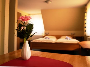 Havergoh Hotel_Doppelzimmer.jpg Zweibettzimmer mit Holzinterieur, Blumen in weißer Vase auf Tisch im Vordergrund, Tageslichtfenster.