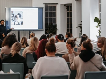BACKYARD LOFT - Tagung Seminarraum mit Vortragendem vor Publikum und Präsentation auf Leinwand.Seminar room with speaker in front of audience and presentation on screen.
