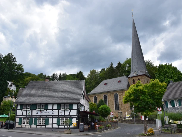 Ensemble Volberg Historisches Fachwerkhaus neben einer alten Kirche mit spitzem Turm unter bewölktem Himmel.