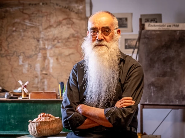Heimatmuseum <p>Älterer Mann mit langem weißem Bart sitzt vor antiker Karte in historisch anmutendem Raum.</p>