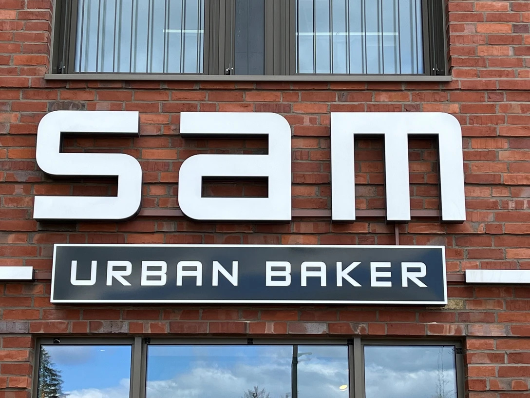 Bäckerei Sam Große, moderne Fassade einer Backstube mit dem Schriftzug "Sam Urban Baker" auf rotem Backstein.