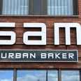 Bäckerei Sam Große, moderne Fassade einer Backstube mit dem Schriftzug "Sam Urban Baker" auf rotem Backstein.