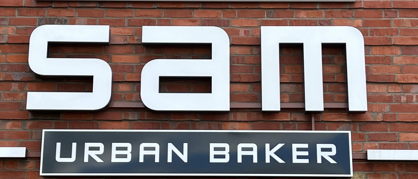 Bäckerei Sam Große, moderne Fassade einer Backstube mit dem Schriftzug "Sam Urban Baker" auf rotem Backstein.