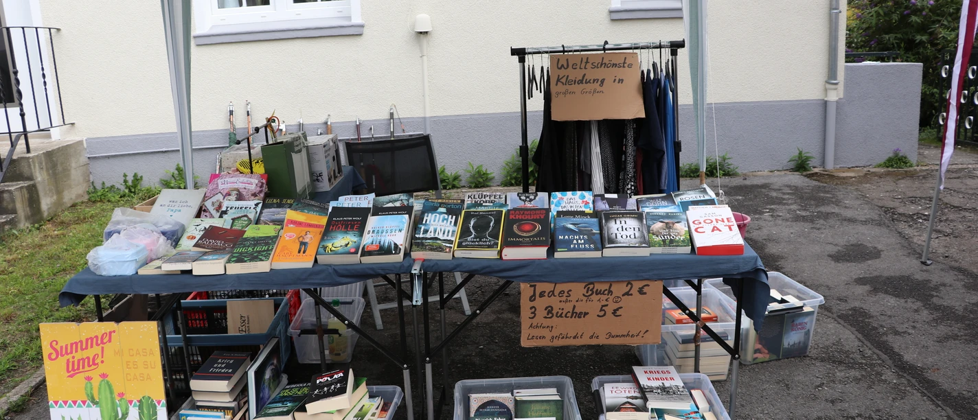Quartierströdel Büchertisch mit Romanen und Kisten voller Bücher unter einem gestreiften Pavillon.