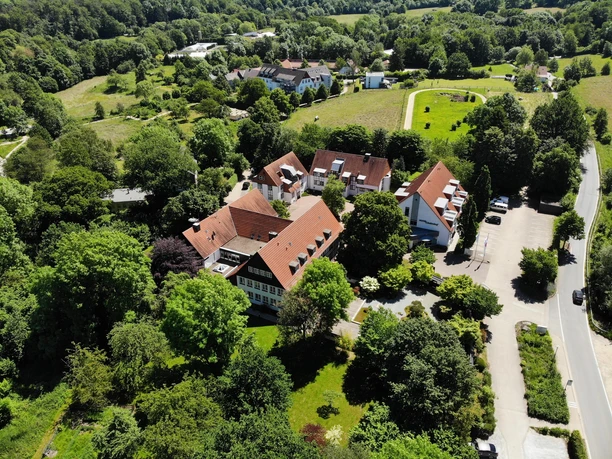 Ein malerisches Anwesen umgeben von grünen Wäldern und Wiesen. Die Architektur ist traditionell mit roten Dächern und einem gepflegten Außenbereich.