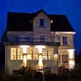 Druckqualität Hoch HAVERGOH-Nacht.jpeg Mehrstöckiges Gästehaus Havergo im Abendrot mit beleuchteten Fenstern und angrenzendem Garten.