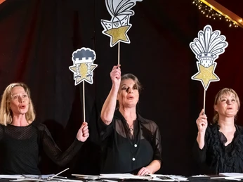 KöNIGE_3-Gestirn Comedy Theater: Drei Frauen stehen auf der Bühne und halten Papierfiguren hoch, die das Dreigestirn darstellen sollenComedy theater: Three women stand on stage and hold up paper figures to represent the triumvirate