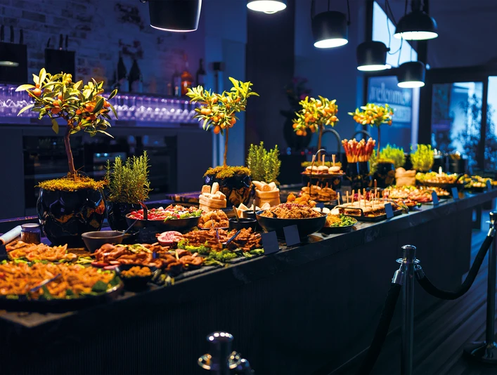 Impressionen Events Dunkler Eventraum, in der Mitte steht ein Tisch mit Catering BuffetDark event room, in the middle is a table with a catering buffet