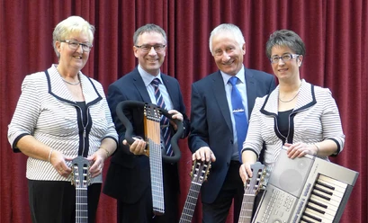 Vielsaitiges Vier Personen stehen vor einem roten Vorhang, drei mit Gitarren, eine mit einem Keyboard.