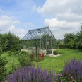 Garten Kottkamp Ein Gewächshaus steht in einem blühenden Garten mit Lavendel im Vordergrund unter einem bewölkten Himmel.