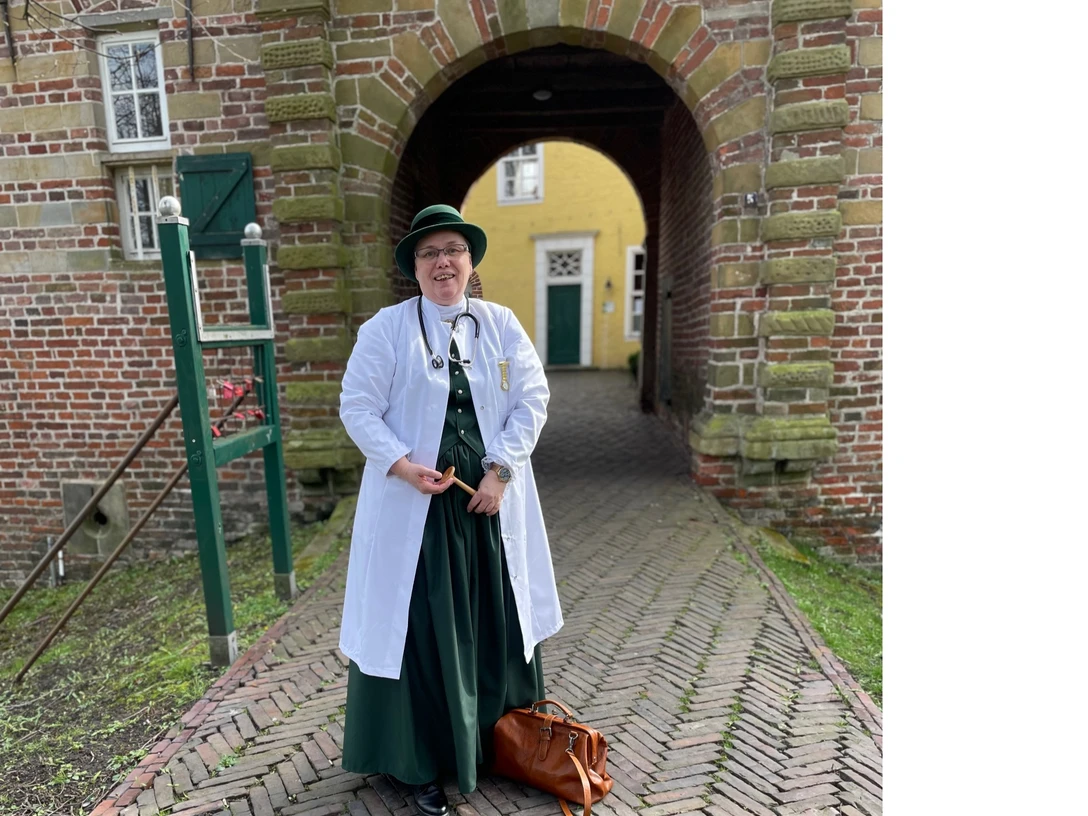 Hermine Heusler-Edenhuizen Frau in historischer Arztkleidung mit Stethoskop und Tasche vor dem Tor der Manningaburg Pewsum