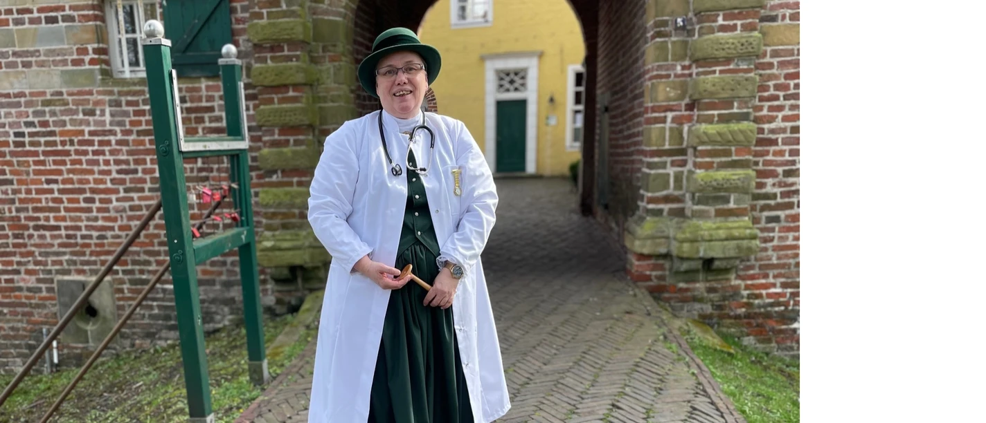 Hermine Heusler-Edenhuizen Frau in historischer Arztkleidung mit Stethoskop und Tasche vor dem Tor der Manningaburg Pewsum