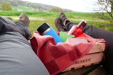 Lienen_Teutoschleife Holperdorper Picknick_Anja Schmidt.jpg Zwei Personen liegen auf einer Wiese, eine Picknickkiste mit Getränken und Decke zwischen ihnen.