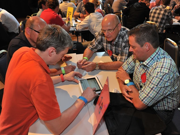 Interaktive Tagung Gruppenarbeit: Vier Männer sitzen an einem Gruppentisch um ein Tablet