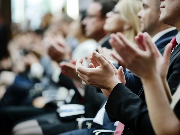 Tagung Klatschende Menschen mit schwarzer Kleidung sitzen in Stuhlreihen