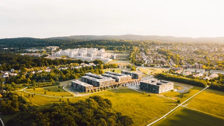Luftaufnahme eines modernen Campus in grüner Umgebung, mit weitläufigen Wiesen und Gebäudekomplex.