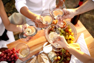 Bad Driburg_Winzerfest_AdobeStock.jpg Weingläser stoßen über einem Tisch voller Trauben, Brot und Käse an, bei einem festlichen Treffen.