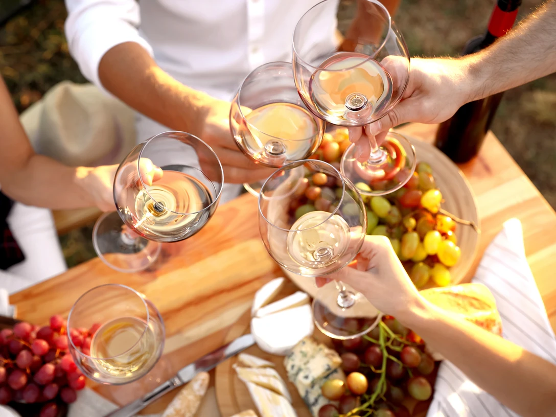 Bad Driburg_Winzerfest_AdobeStock.jpg Weingläser stoßen über einem Tisch voller Trauben, Brot und Käse an, bei einem festlichen Treffen.