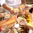 Bad Driburg_Winzerfest_AdobeStock.jpg Weingläser stoßen über einem Tisch voller Trauben, Brot und Käse an, bei einem festlichen Treffen.