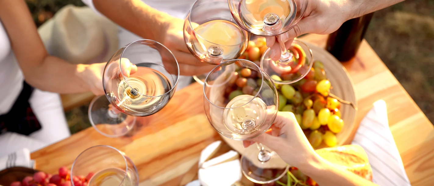 Bad Driburg_Winzerfest_AdobeStock.jpg Weingläser stoßen über einem Tisch voller Trauben, Brot und Käse an, bei einem festlichen Treffen.