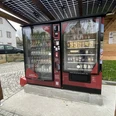 Proviantomat Standort in Schöna Roter Verkaufsautomat unter Solardach, gefüllt mit Getränken und Snacks, steht auf gepflastertem Platz neben einem Haus und Holzwand.Red vending machine under a solar roof, filled with drinks and snacks, stands on a paved square next to a house and wooden wall.Červený automat pod solární střechou, plný nápojů a občerstvení, stojí na dlážděném náměstí vedle domu a dřevěné zdi.Czerwony automat pod słonecznym dachem, wypełniony napojami i przekąskami, stoi na wybrukowanym placu obok domu i drewnianej ściany.Een rode automaat onder een zonnedak, gevuld met drankjes en snacks, staat op een geplaveid plein naast een huis en een houten muur.Un distributore automatico rosso sotto un tetto solare, pieno di bevande e snack, si trova su una piazza lastricata accanto a una casa e a un muro di legno.