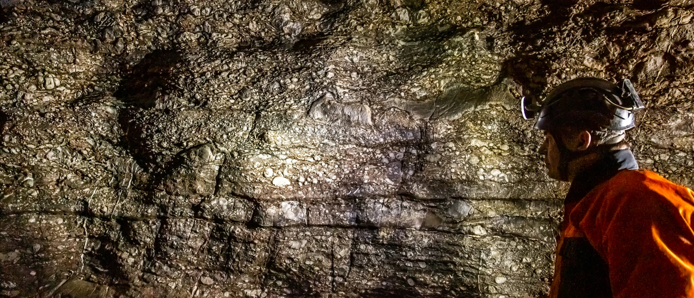 Aggertalhöhle Ein Höhlenforscher betrachtet gebannt die strukturierte Felswand in einer dunklen Höhlenkammer.