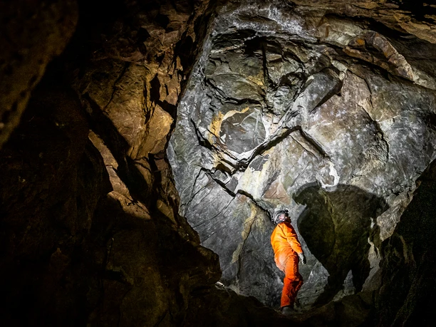 Aggertalhöhle Höhlenforscher in orange steht in beleuchteter Felsgrotte mit beeindruckenden Steinstrukturen.