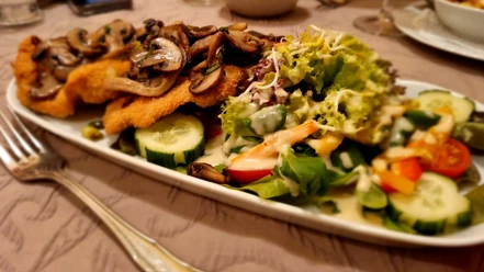 Holter_Krüstchen_CC_BY_SA_Teutoburger_Wald_Stadt_Schloss_Holte-Stukenbrock.jpg Panierte Schnitzel mit gebratenen Pilzen, angerichtet auf einem Teller neben frischem Salat.