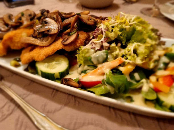 Holter_Krüstchen_CC_BY_SA_Teutoburger_Wald_Stadt_Schloss_Holte-Stukenbrock.jpg Panierte Schnitzel mit gebratenen Pilzen, angerichtet auf einem Teller neben frischem Salat.