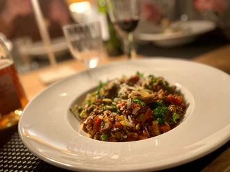Ein Teller mit Spaghetti Bolognese, angerichtet mit Petersilie und Parmesan auf einem gedeckten Tisch.