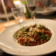 Ein Teller mit Spaghetti Bolognese, angerichtet mit Petersilie und Parmesan auf einem gedeckten Tisch.