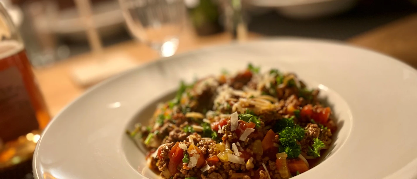 Ein Teller mit Spaghetti Bolognese, angerichtet mit Petersilie und Parmesan auf einem gedeckten Tisch.
