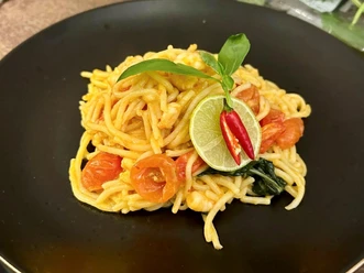 Spaghetti auf schwarzem Teller, garniert mit Tomaten, Limettenscheiben, Chili und einem frischen Basilikumblatt.
