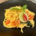 Spaghetti auf schwarzem Teller, garniert mit Tomaten, Limettenscheiben, Chili und einem frischen Basilikumblatt.
