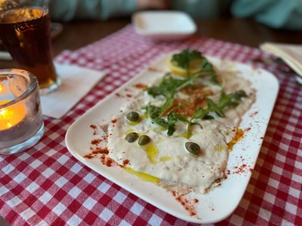 Ein Teller Vitello Tonnato mit Kapern und Rucola auf rot-weiß kariertem Tischtuch angerichtet.