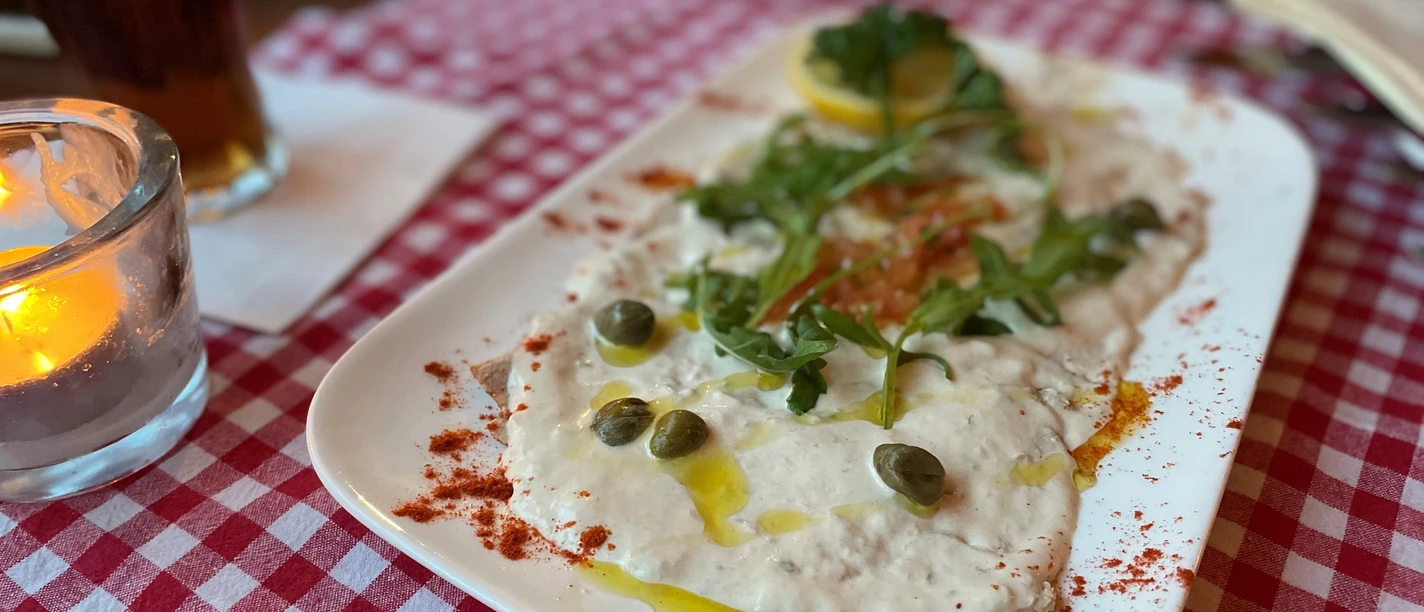 Ein Teller Vitello Tonnato mit Kapern und Rucola auf rot-weiß kariertem Tischtuch angerichtet.