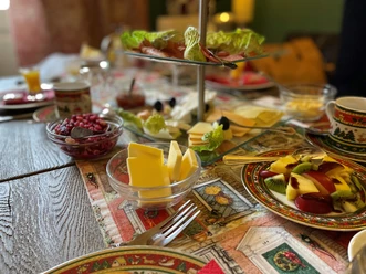 Vielfältiges Frühstück mit Obst, Käse, Brötchen und Wurst auf buntem Tischgedeck im Tageslicht.
