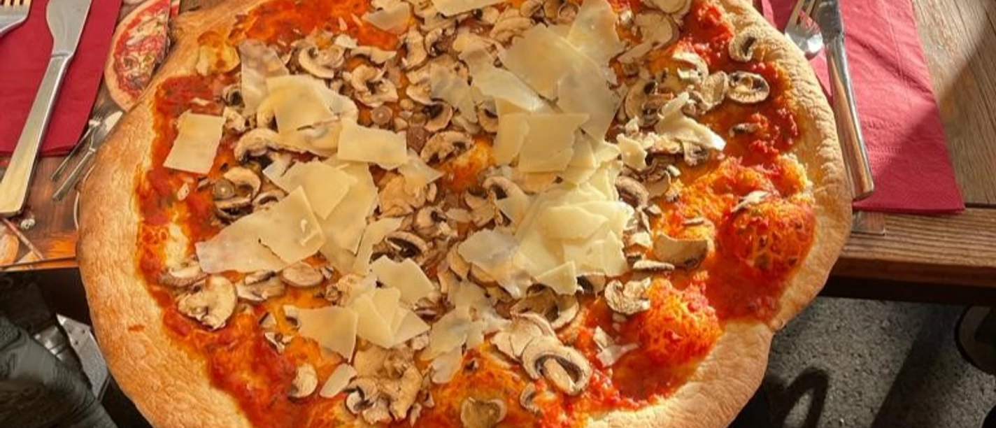 Pizza mit reichlich Tomatensoße, frischen Champignons und großzügigen Käsestreifen auf knusprigem Boden.