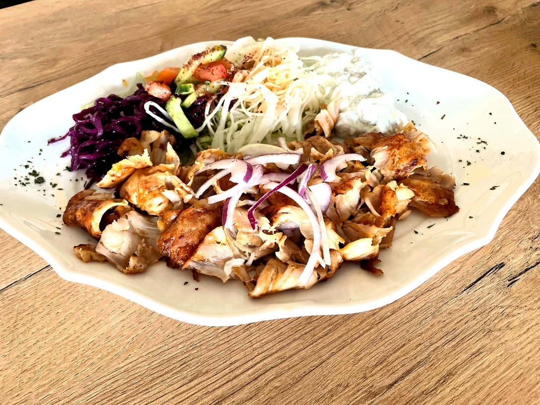 ZZZ_32CC-BY-SA_Teutoburger_Wald_Stadt_Schloß_Holte-Stukenbrock.jpg Ein Teller mit saftigem Hähnchen, roter Zwiebel, Krautsalat, Weißkraut und Zaziki auf rustikalem Holztisch.