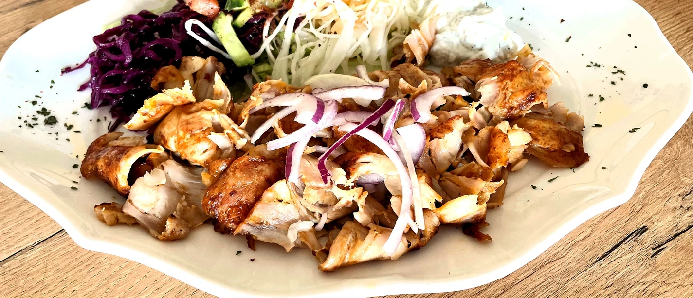 ZZZ_32CC-BY-SA_Teutoburger_Wald_Stadt_Schloß_Holte-Stukenbrock.jpg Ein Teller mit saftigem Hähnchen, roter Zwiebel, Krautsalat, Weißkraut und Zaziki auf rustikalem Holztisch.