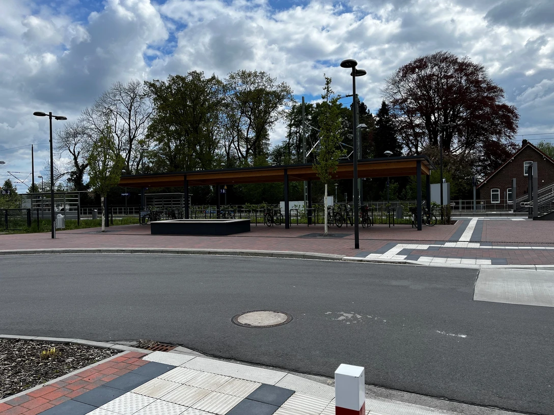 Überdachte Fahrradstellplätze am Bahnhof.jpg Überdachte Fahrradstellplätze am Bahnhof, mit modernen Strukturen, beleuchtet bei Tageslicht. Im Hintergrund sind Bäume und ein Gebäude erkennbar.