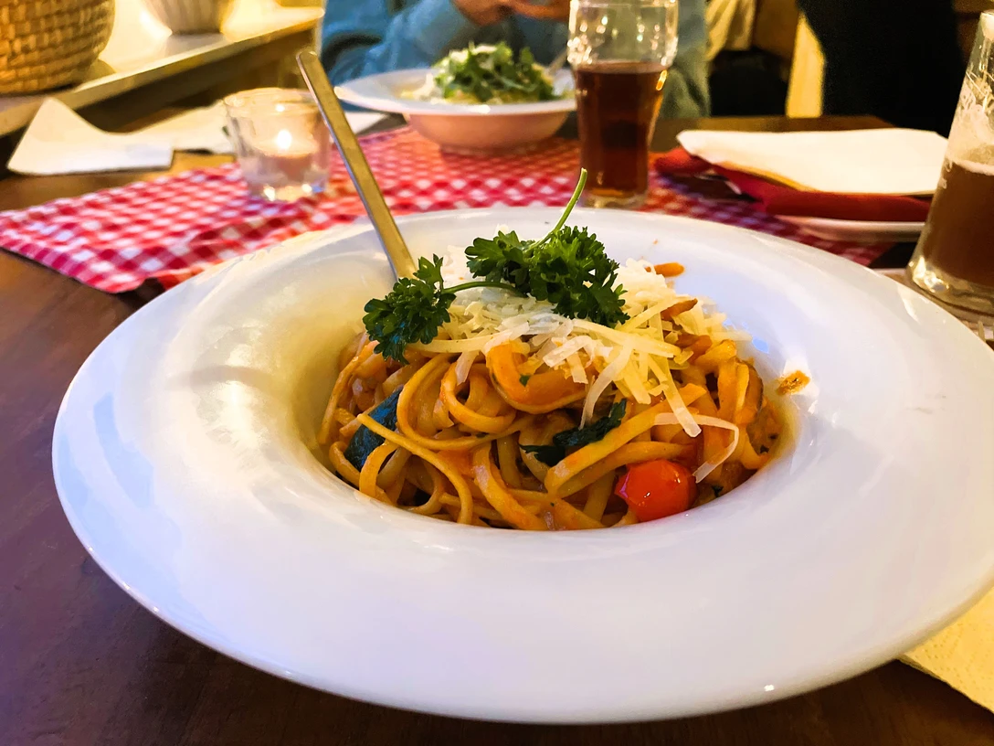 Ein Teller Spaghetti mit Tomatensauce, frischem Basilikum und geriebenem Käse, serviert auf Holzttisch.