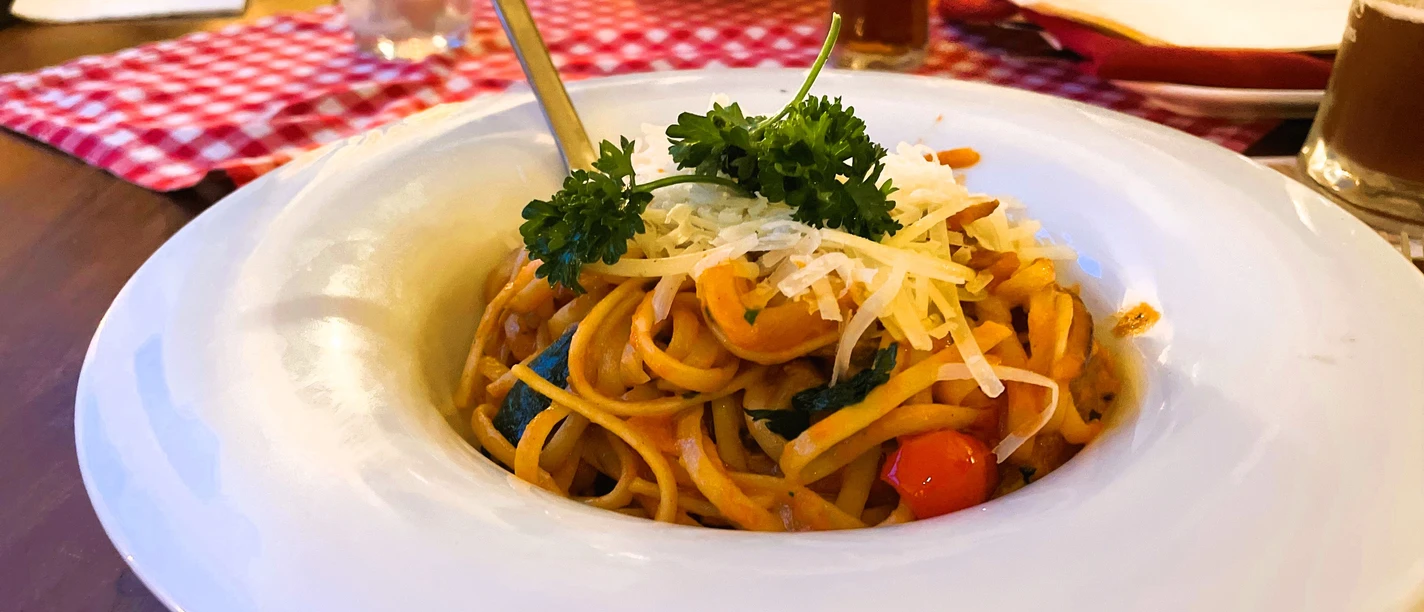 Ein Teller Spaghetti mit Tomatensauce, frischem Basilikum und geriebenem Käse, serviert auf Holzttisch.