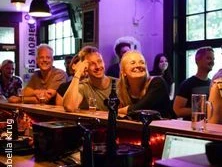 Eine fröhliche Gruppe von Menschen an einer Theke in stimmungsvoller Beleuchtung einer Bar.