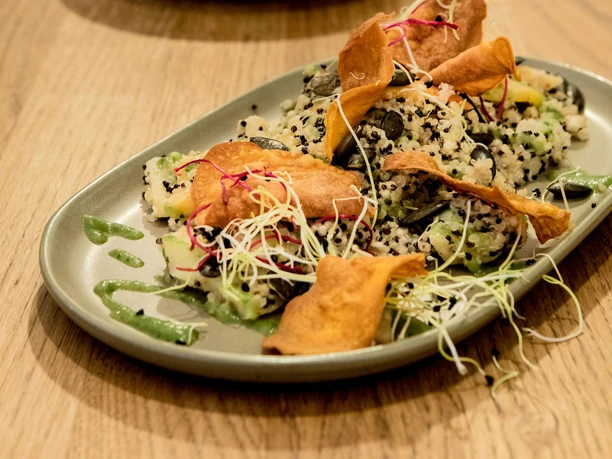 Tigermilch An exquisitely plated gourmet dish featuring quinoa and crispy sweet potato chips, presented on a wooden table.