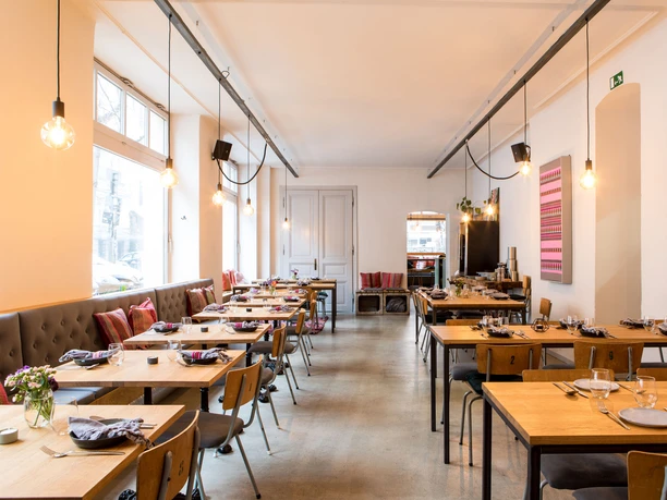 Tigermilch Cozy restaurant featuring wooden furnishings, open lighting, and colorful artwork adorning the walls.