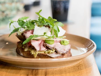 Neobiota Ein kunstvoll angerichtetes Tellergericht mit zartem Roastbeef, Rucola und Parmesanspänen auf einem Holztisch.An artfully arranged plate with tender roast beef, rocket and Parmesan shavings on a wooden table.