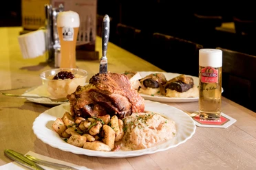 Hellers Brauhaus Ein gedeckter Tisch mit verschiedenen deftig mächtigen Speisen und ein Glas Kölsch-