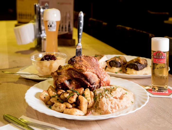 Hellers Brauhaus Ein gedeckter Tisch mit verschiedenen deftig mächtigen Speisen und ein Glas Kölsch-A table set with a variety of hearty dishes and a glass of Kölsch beer.